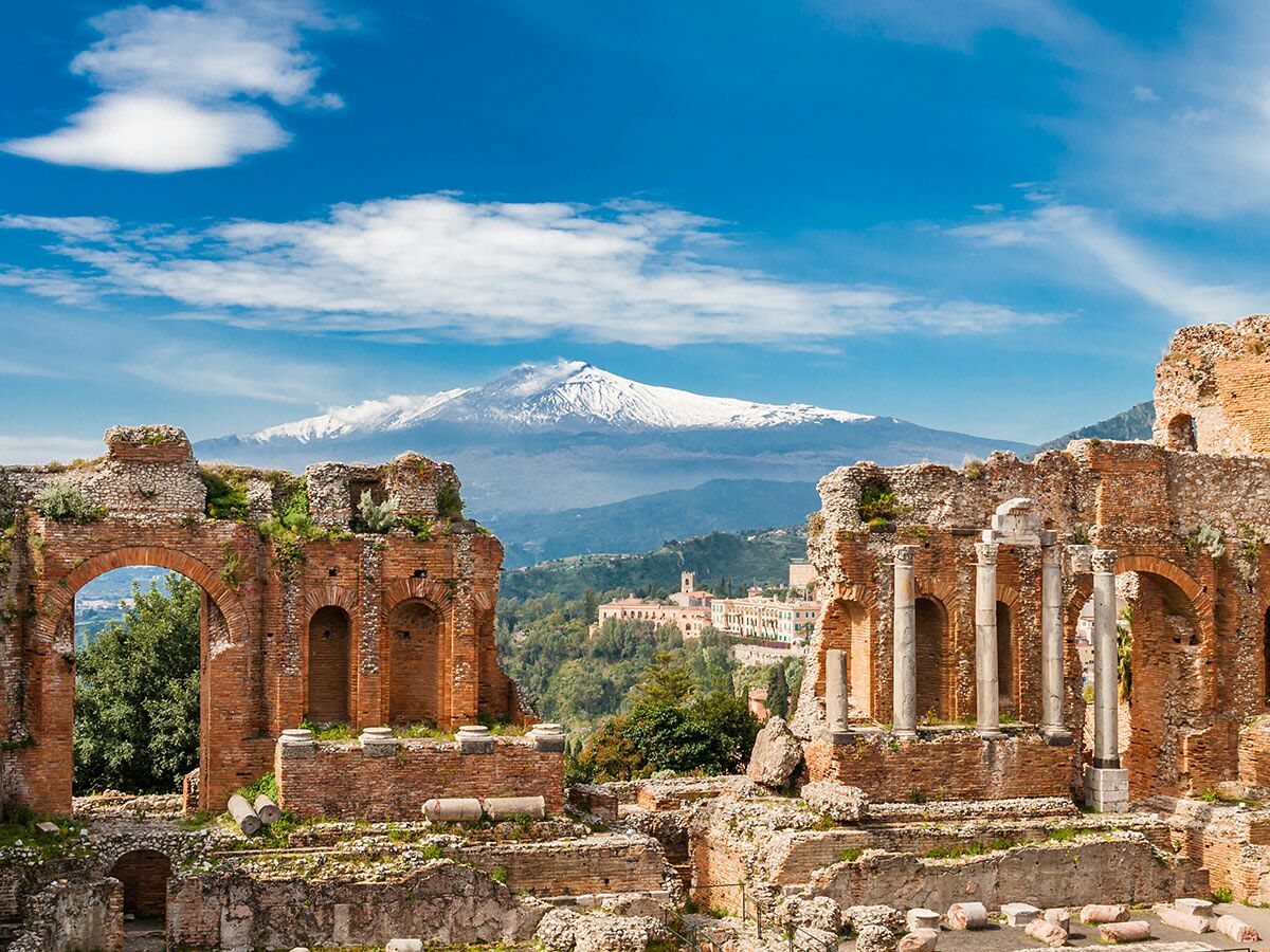 Antike römische oder griechische Ruinen (Theater) in Taormina, Sizilien, mit dem schneebedeckten Vulkan Ätna im Hintergrund unter blauem Himmel.