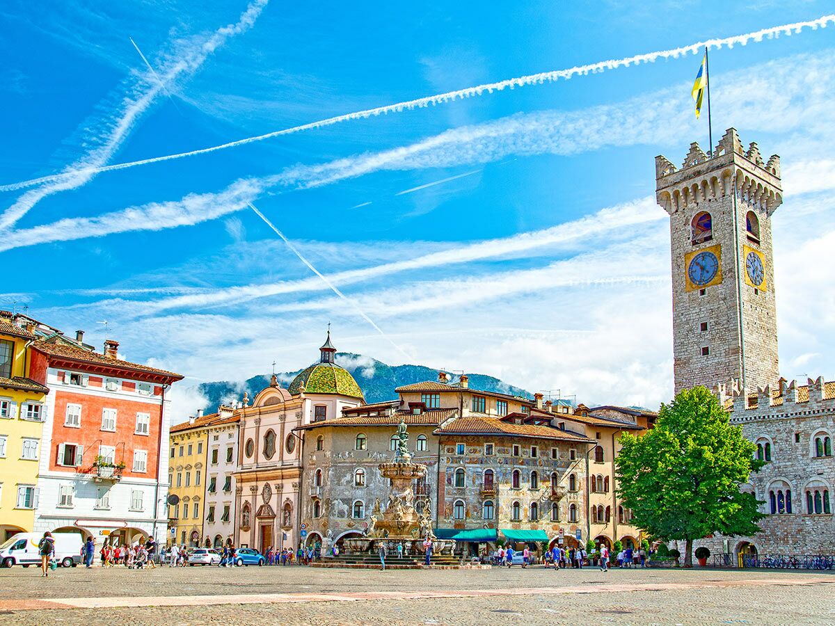 Panoramablick auf den sonnigen Stadtplatz Piazza Duomo in Trento, Italien, mit dem Uhrturm, Neptunbrunnen und historischen Gebäuden.