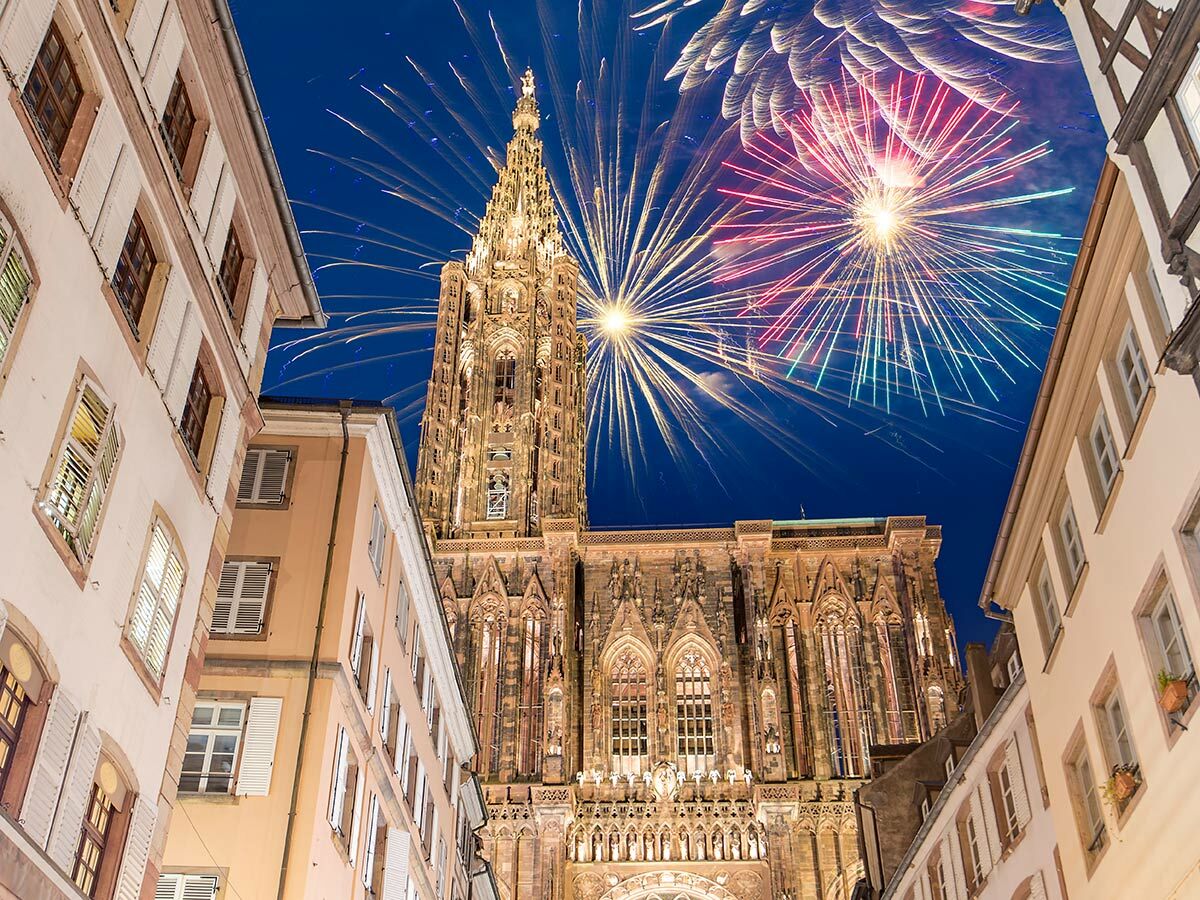 Das Straßburger Münster bei Nacht, umrahmt von historischen Gebäuden, mit farbenprächtigen Feuerwerken am Himmel.
