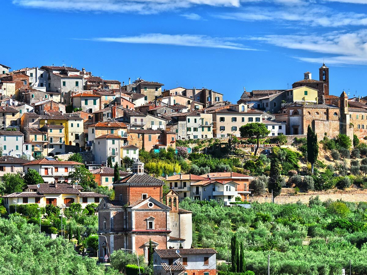 Panoramablick auf eine malerische italienische Hügelstadt mit bunten Häusern, Kirchen und Olivenhainen unter blauem Himmel.