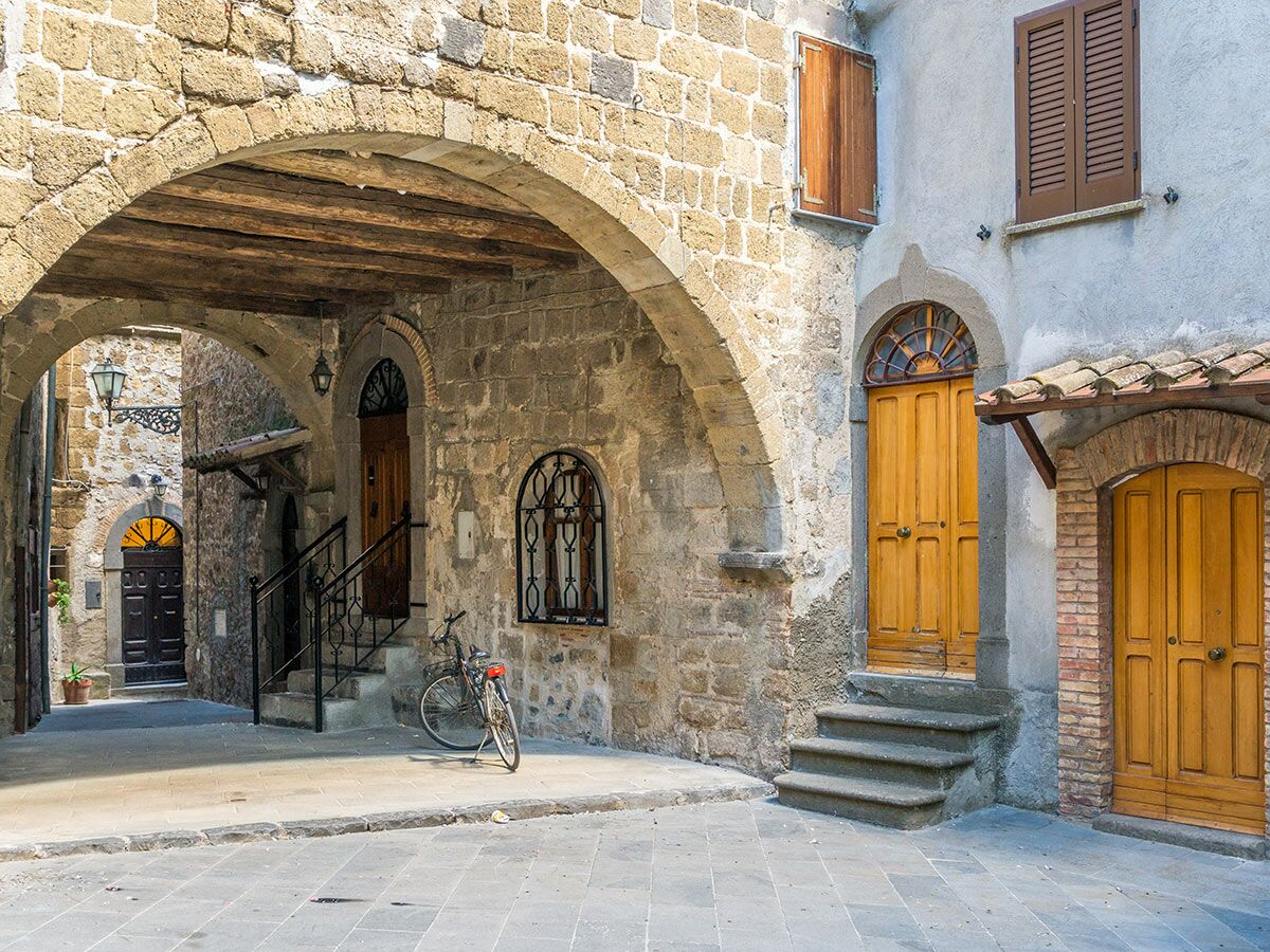 Charmante Gasse in einer italienischen Altstadt mit Steinbögen, historischen Holztüren und einem Fahrrad am Straßenrand.