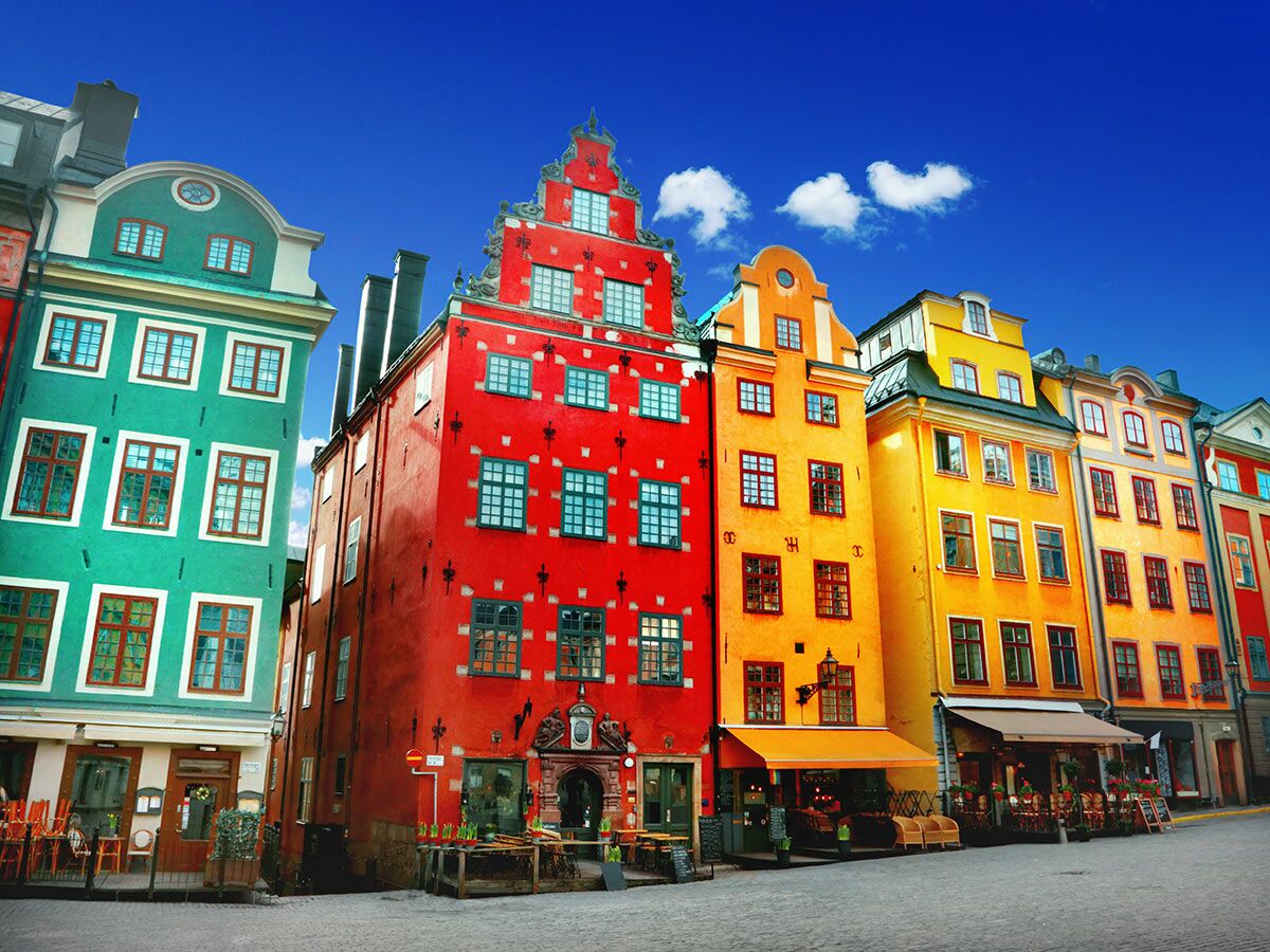 Lebhafte farbige historische Gebäude in Gamla Stan, Stockholm, Schweden, säumen eine Kopfsteinpflasterstraße unter blauem Himmel.