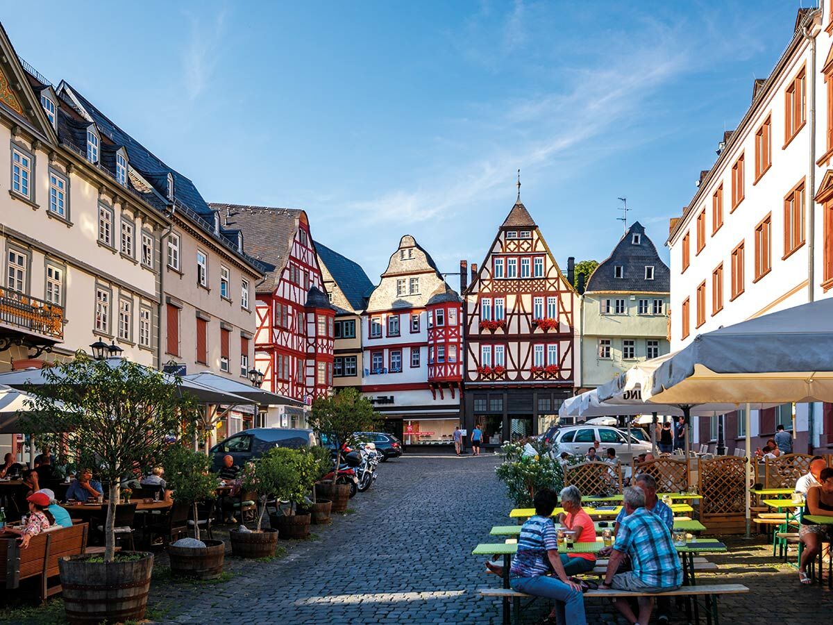 Lebhafter deutscher Stadtplatz mit farbenfrohen Fachwerkhäusern, Kopfsteinpflaster und Menschen, die in Straßencafés entspannen.