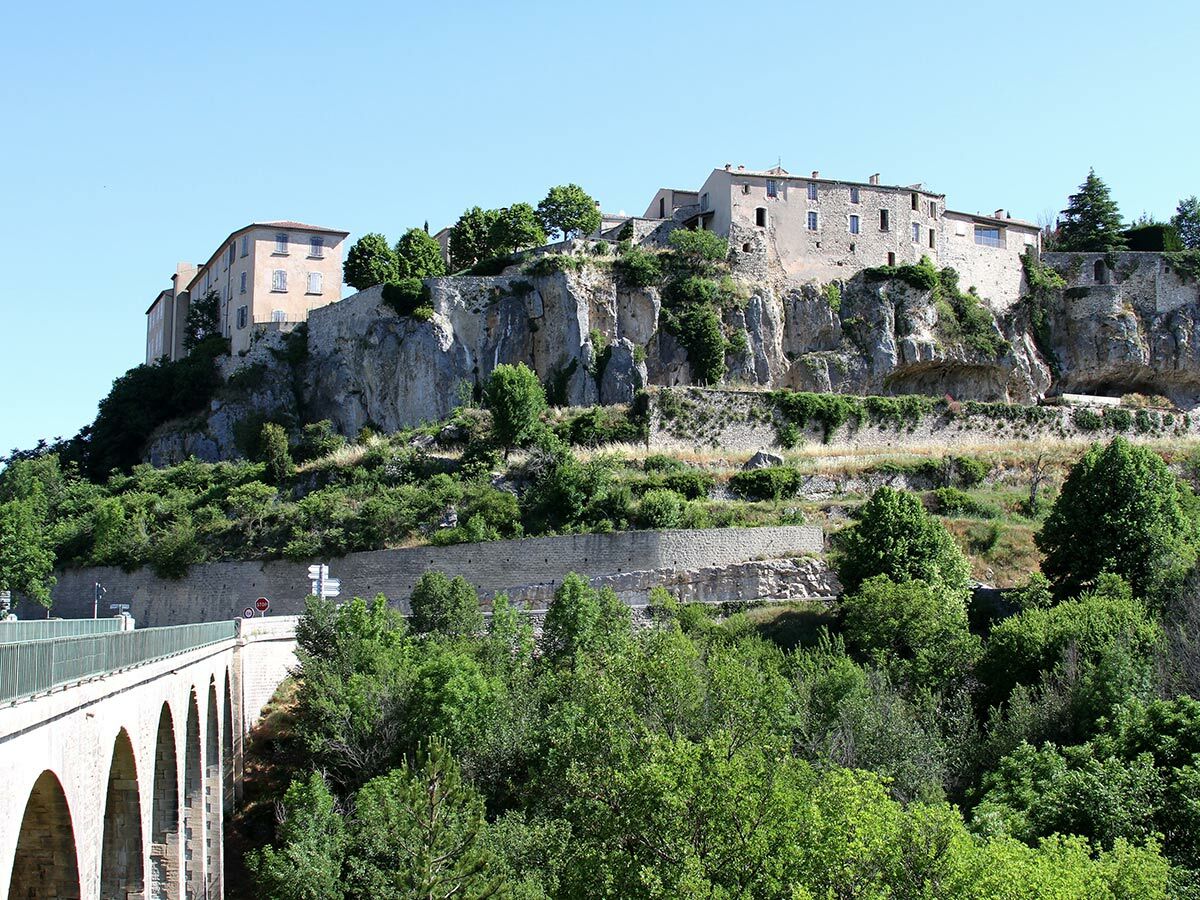 Blick auf die historische Felsenstadt Vaison-la-Romaine in der Provence mit alten Steinhäusern und einer Bogenbrücke.