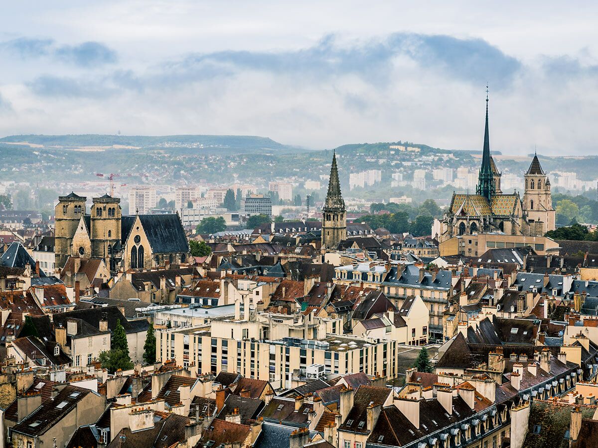 Panoramaansicht der historischen Stadt Dijon, Frankreich, mit zahlreichen Dächern, Kirchtürmen und Kathedralen unter bewölktem Himmel.