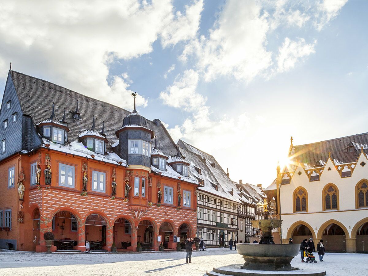 Sonnenbeschienener historischer Marktplatz in Deutschland im Winter, mit Schnee auf Dächern, belebten Gebäuden und Brunnen.