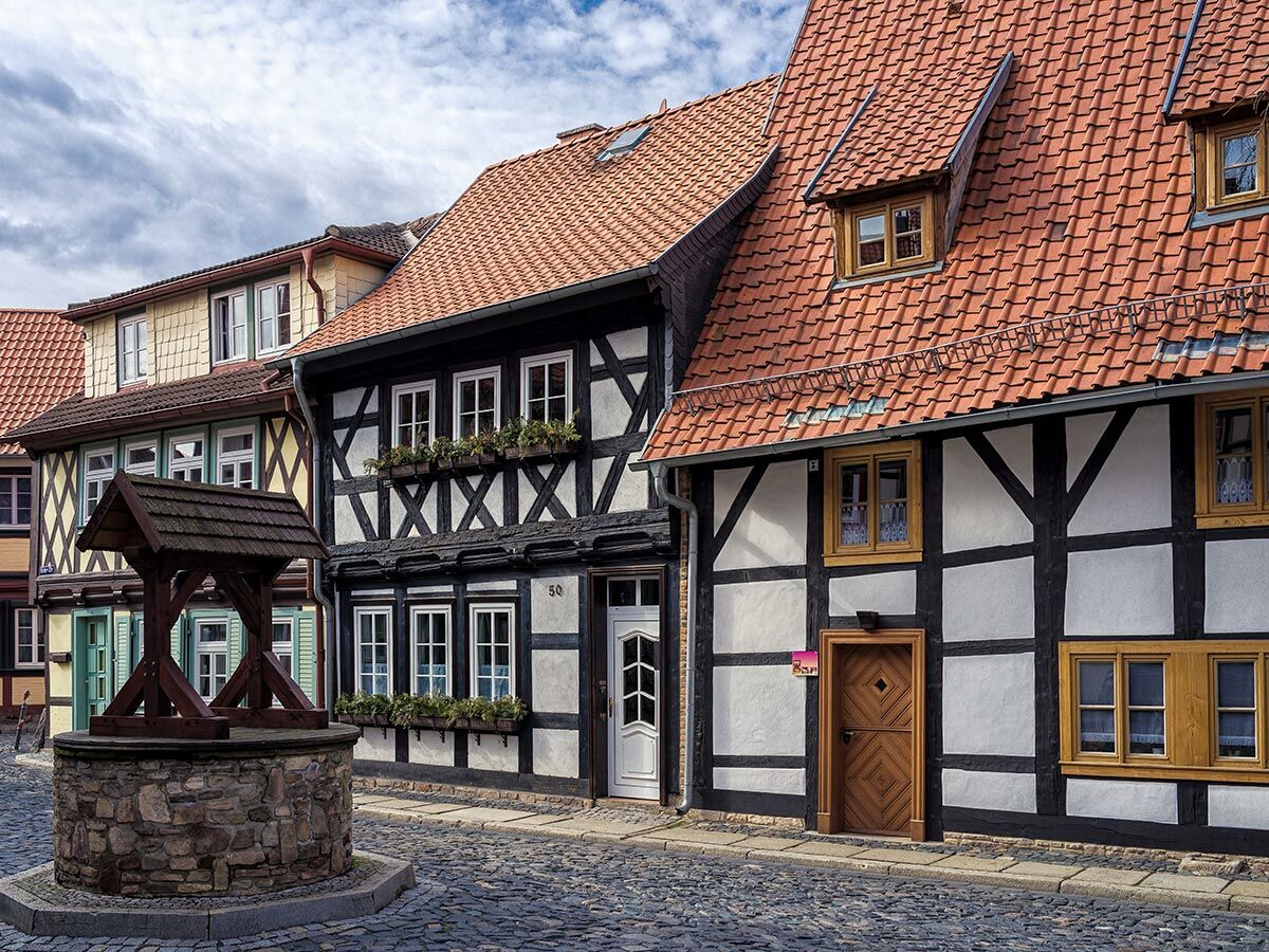 Historische Fachwerkhäuser mit roten Ziegeldächern und Holzbalken an einer Kopfsteinpflastergasse mit altem Brunnen.