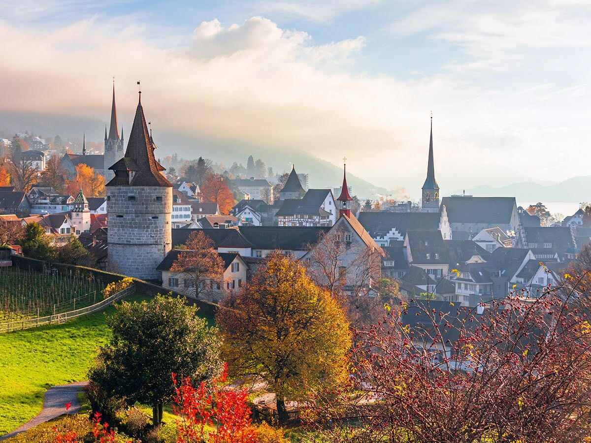 Malerische Schweizer Altstadt mit historischem Turm, Kirchen und bunten Herbstbäumen im goldenen Morgenlicht.