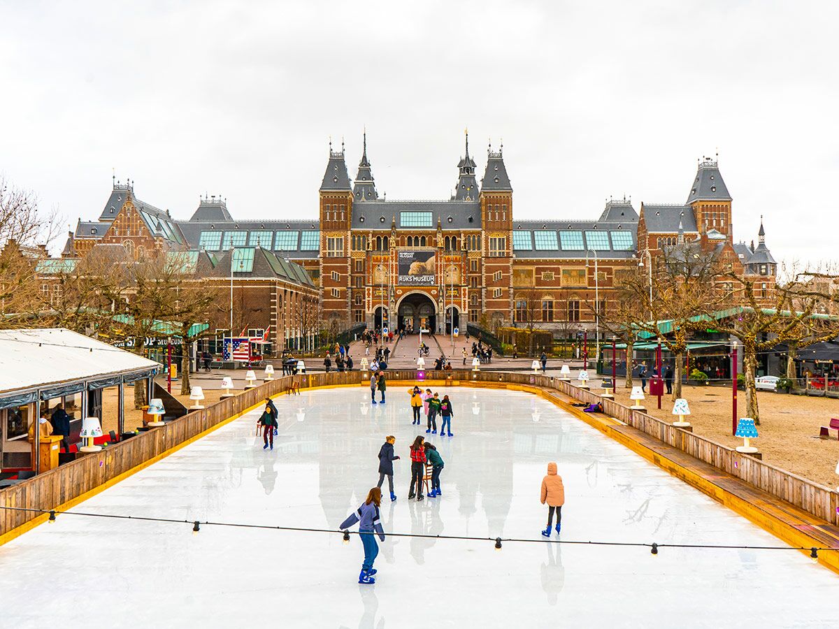 Menschen beim Eislaufen auf einer Eisbahn vor dem Rijksmuseum in Amsterdam im Winter, mit beeindruckender Architektur.