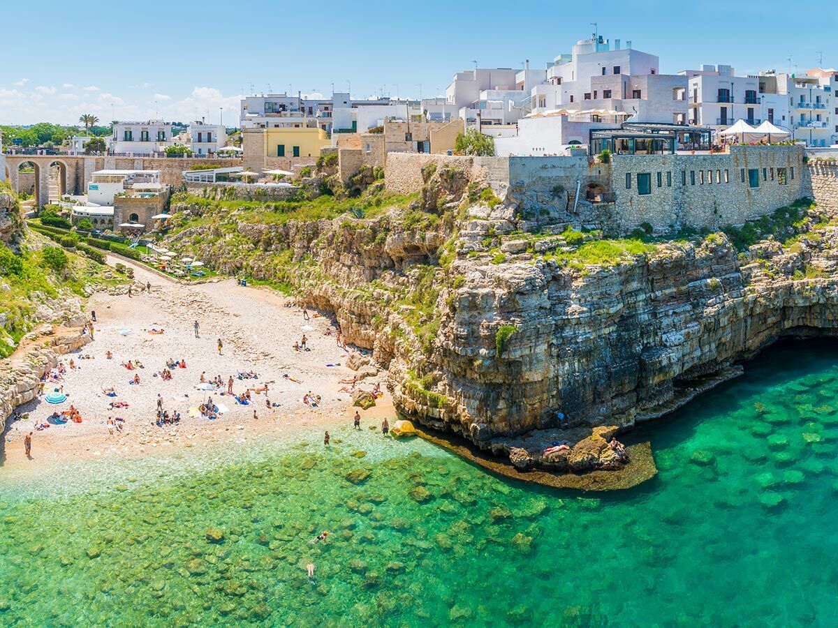 Blick auf den Strand Lama Monachile in Polignano a Mare, Italien, mit weißgetünchten Häusern und Felsenküste.