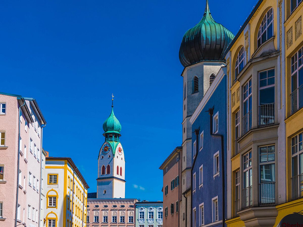 Bunte Gebäude und historische Kirchtürme mit Zwiebelhauben vor blauem Himmel in einer malerischen Altstadt.