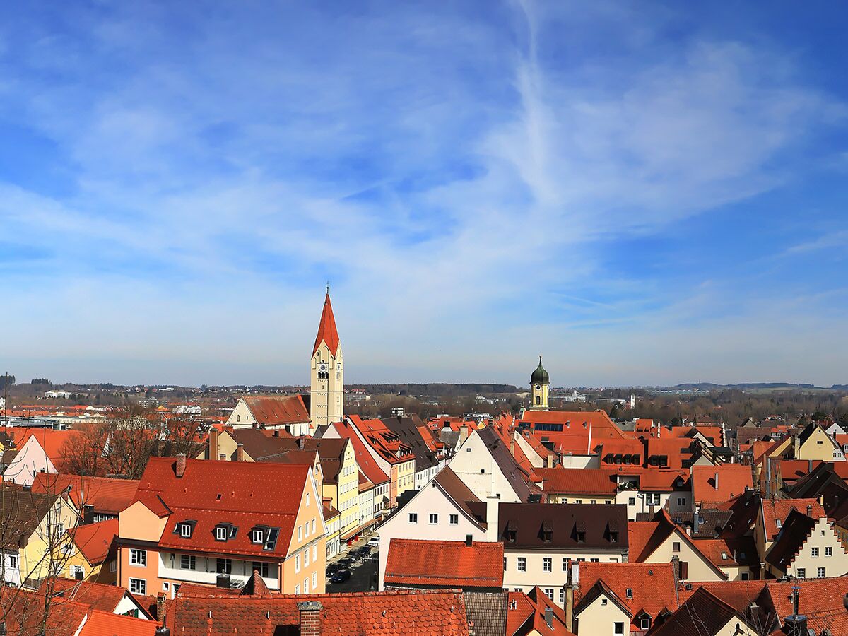 Panoramablick auf historische Stadt mit roten Ziegeldächern, Kirchtürmen und blauem Himmel in Europa.