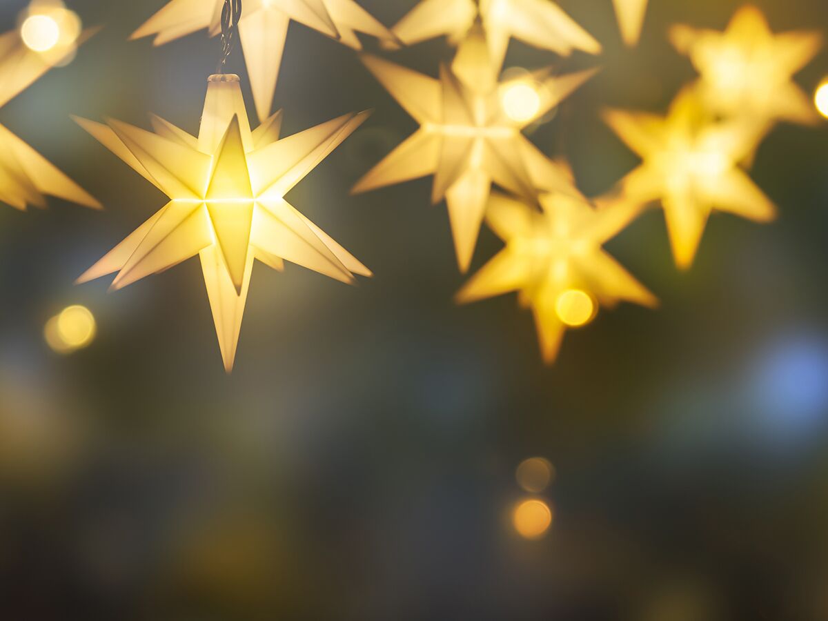 Nahaufnahme von leuchtenden gelben Papiersternen vor dunklem, unscharfem Hintergrund mit Bokeh-Lichtern, festliche Dekoration.