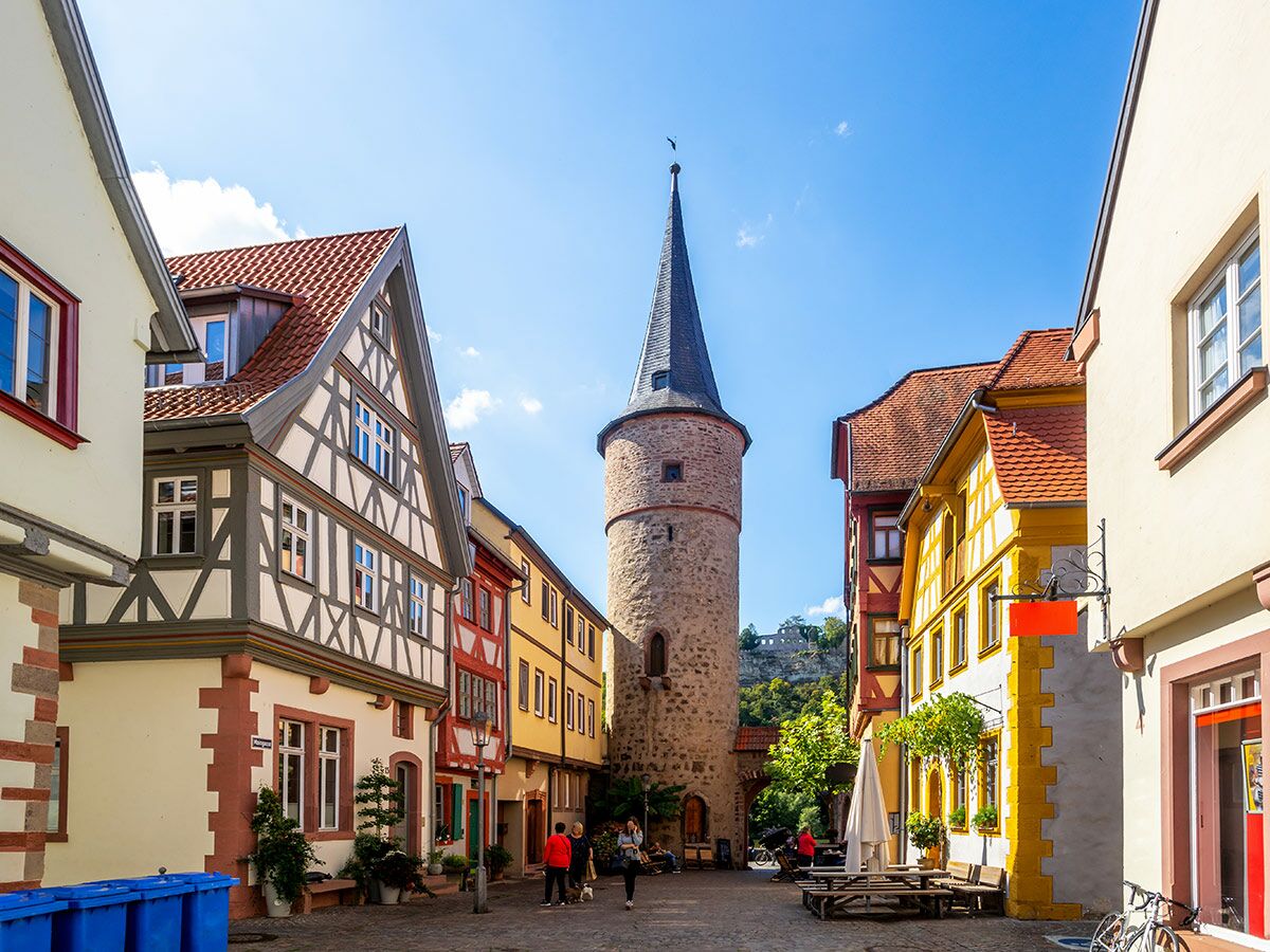 Historische Altstadt Gelnhausen mit malerischen Fachwerkhäusern, Kopfsteinpflastergasse, mittelalterlichem Turm und Fußgängern bei Sonnenschein.