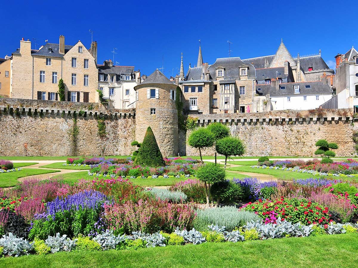 Farbenprächtiger Garten vor der historischen Stadtmauer mit Turm und alten Gebäuden in Vannes, Bretagne, Frankreich.
