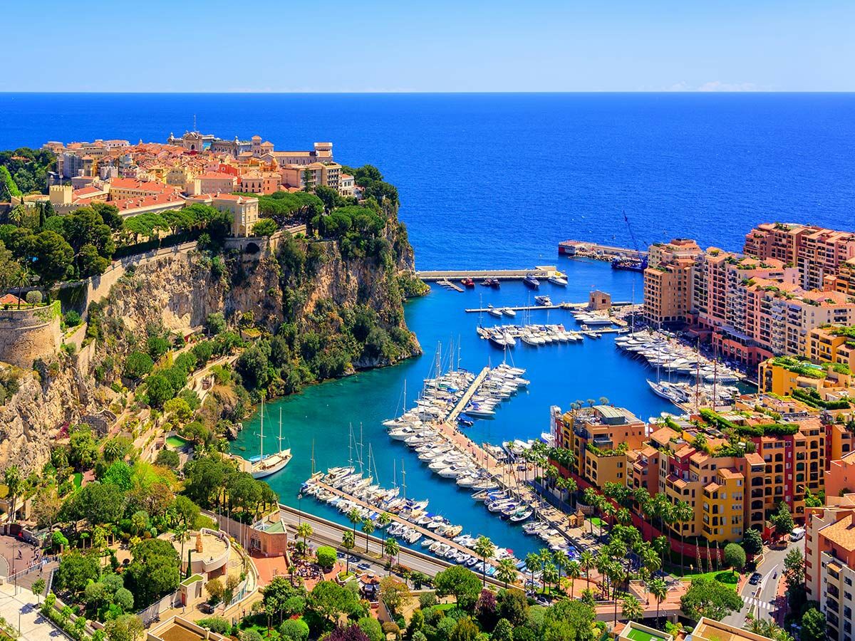 Panoramablick auf Monacos Port Hercule, Luxusyachten im Hafen und farbenfrohe Gebäude am Felsen der Côte d'Azur.