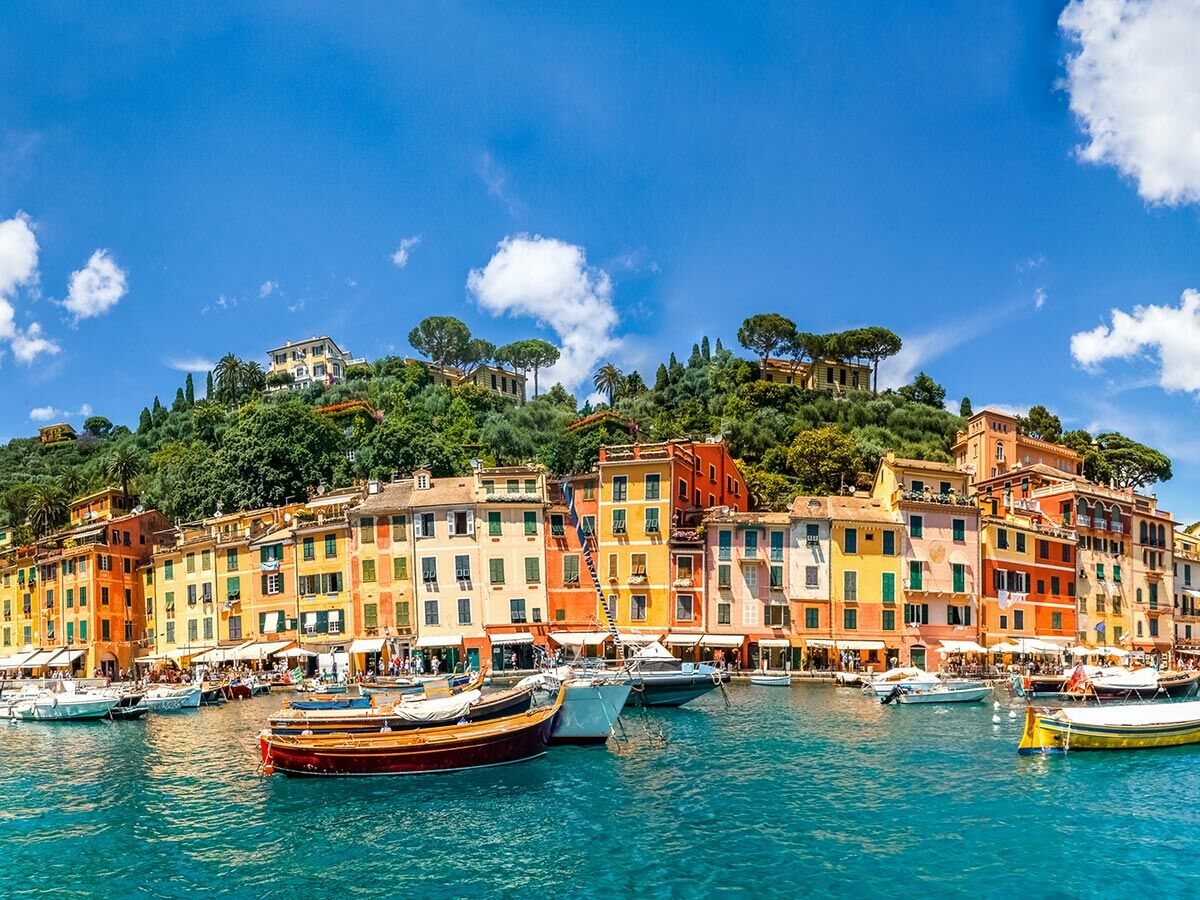 Panoramablick auf Portofino, Italien: Bunte Häuser am Hafen, grüne Hügel und Boote im türkisfarbenen Wasser unter blauem Himmel.