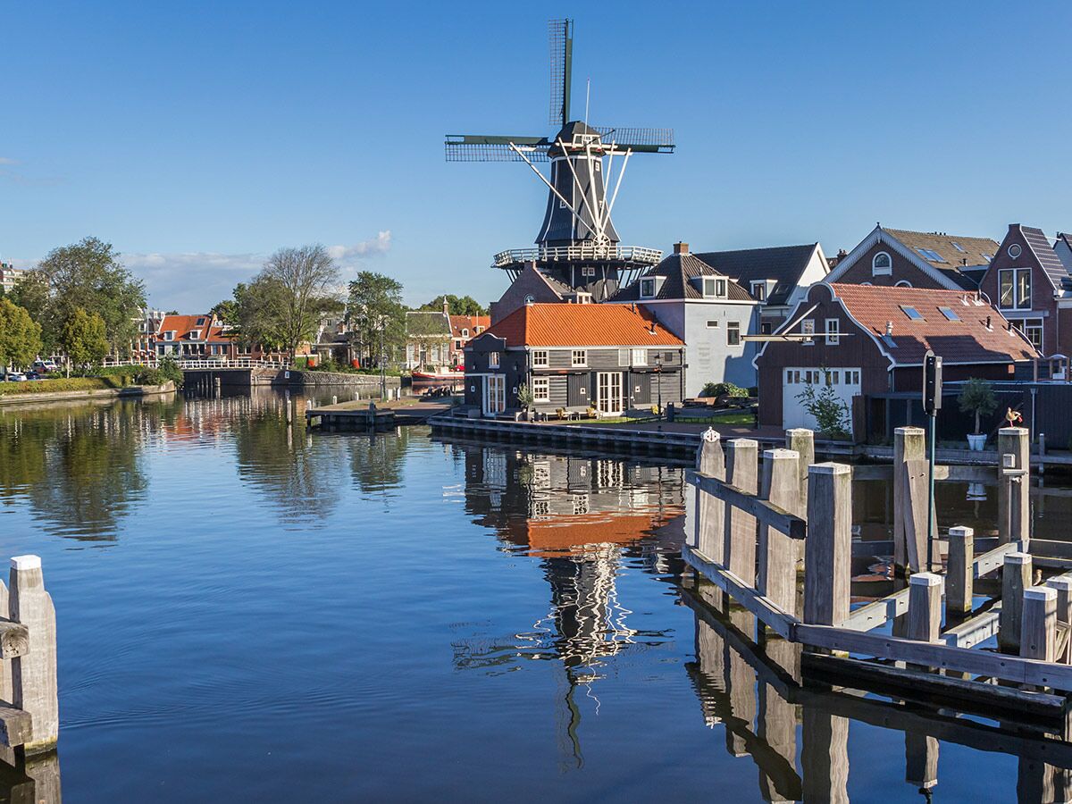 Blick auf historische holländische Windmühle und bunte Häuser entlang eines Kanals an einem sonnigen Tag mit klarem Himmel.