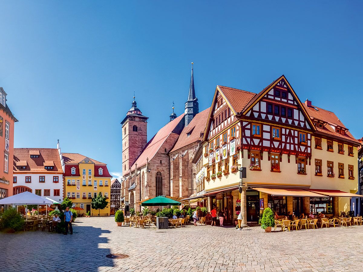 Sonniger Marktplatz in einer deutschen Altstadt mit historischen Fachwerkhäusern, einer Kirche und belebten Straßencafés.