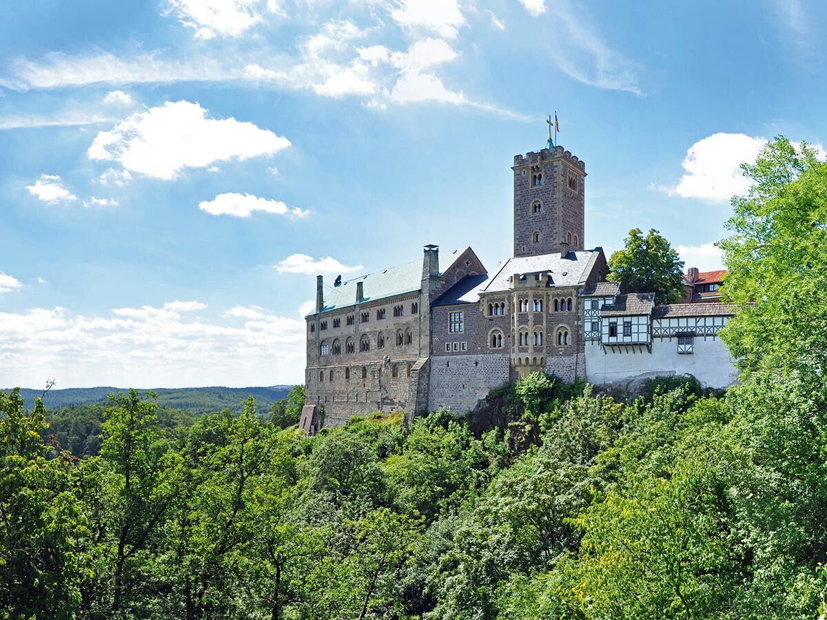 Historisches Wartburg Schloss in Eisenach, Deutschland, auf einem bewaldeten Hügel unter blauem Himmel mit weißen Wolken.
