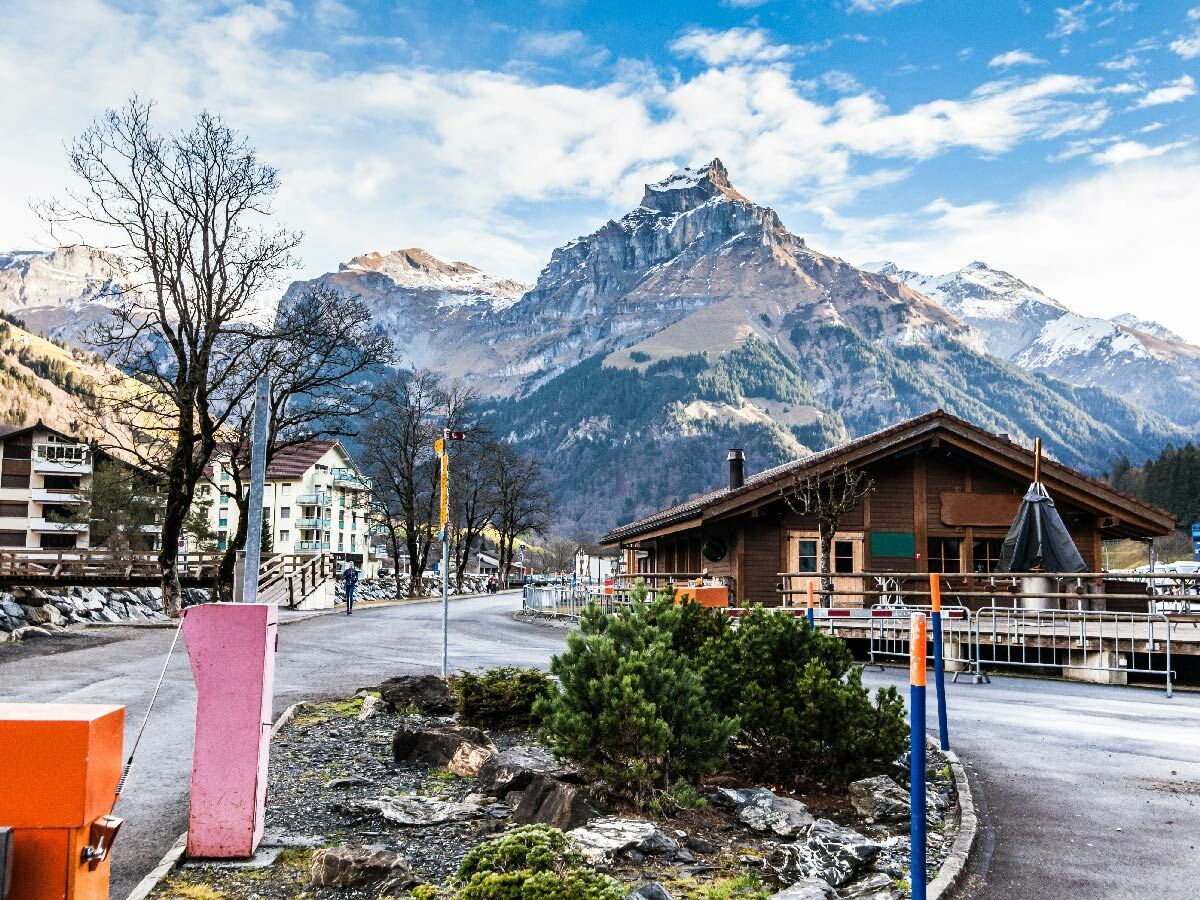 Panoramablick auf ein charmantes Bergdorf in den Schweizer Alpen mit traditionellen Chalets und schneebedeckten Gipfeln unter blauem Himmel.