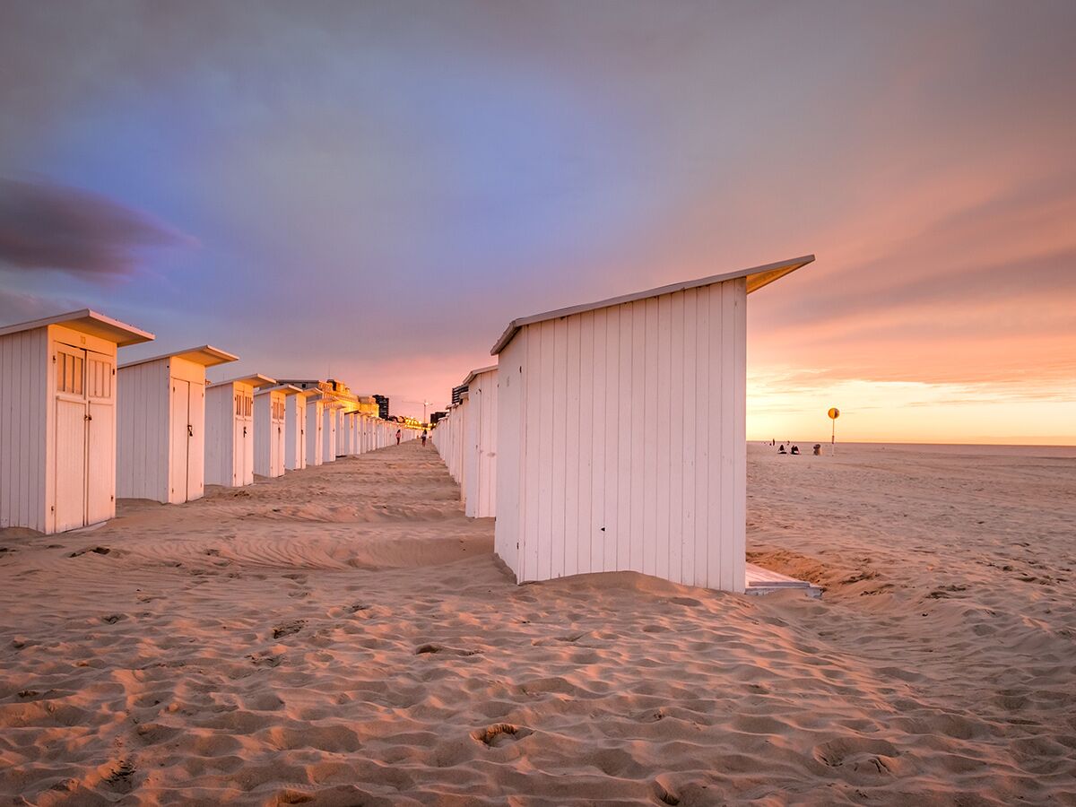 Weiße Strandhütten säumen einen sandigen Strand unter einem farbenprächtigen Sonnenuntergangshimmel.