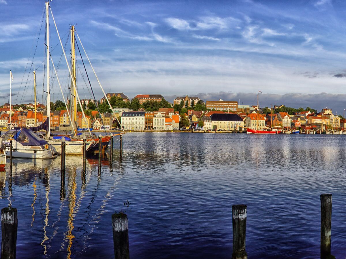 Malerische Hafenstadt mit bunten Gebäuden und Segelbooten im Hafen, blauer Himmel. Idyllischer Ausblick am Wasser.