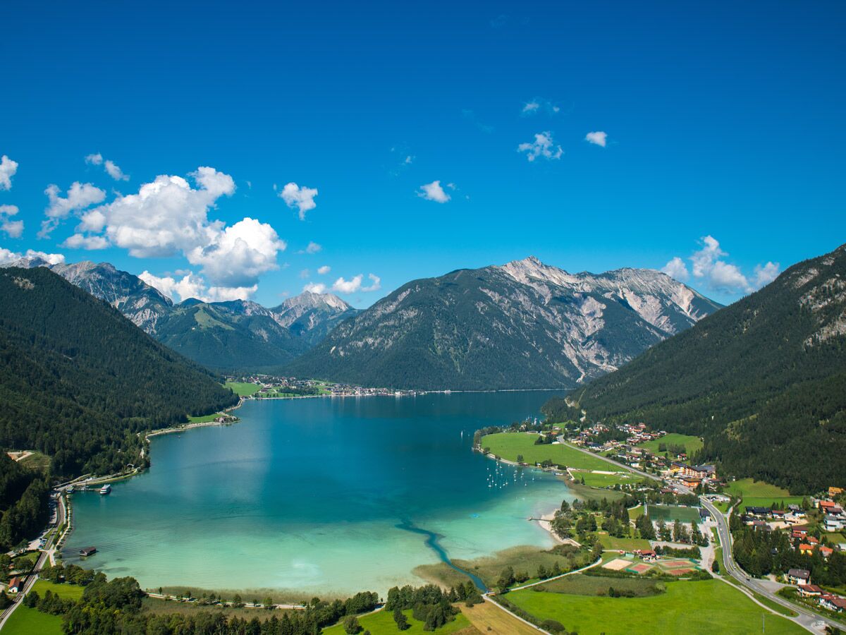 Panoramablick auf den Achensee in Tirol, Österreich, umgeben von bewaldeten Alpen und idyllischen Bergdörfern unter blauem Himmel.