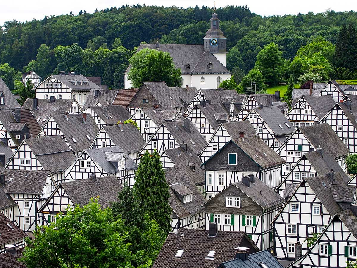 Malerisches Dorf mit traditionellen schwarz-weißen Fachwerkhäusern, grauen Dächern und einer historischen Kirche im grünen Wald.