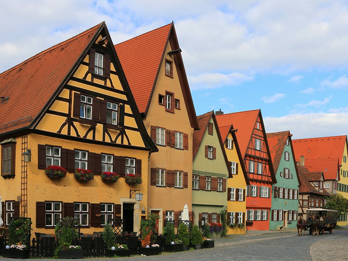Reihe bunter historischer Fachwerkhäuser mit roten Dächern in Rothenburg ob der Tauber, Pferdekutsche auf Kopfsteinpflasterstraße.