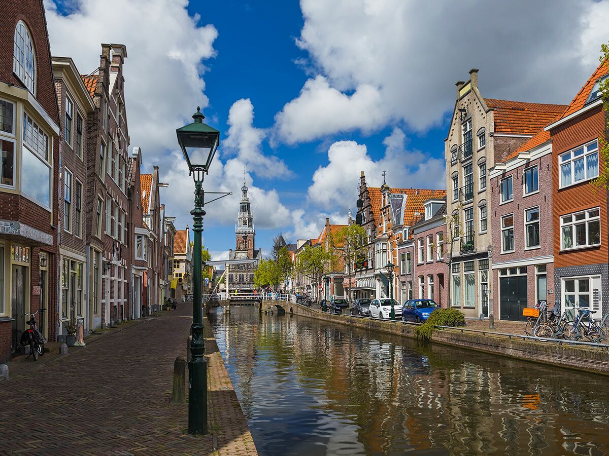 Historische Gracht in Alkmaar, Niederlande, mit traditionellen Häusern, Kanal und dem Waag-Gebäude im Hintergrund unter blauem Himmel.