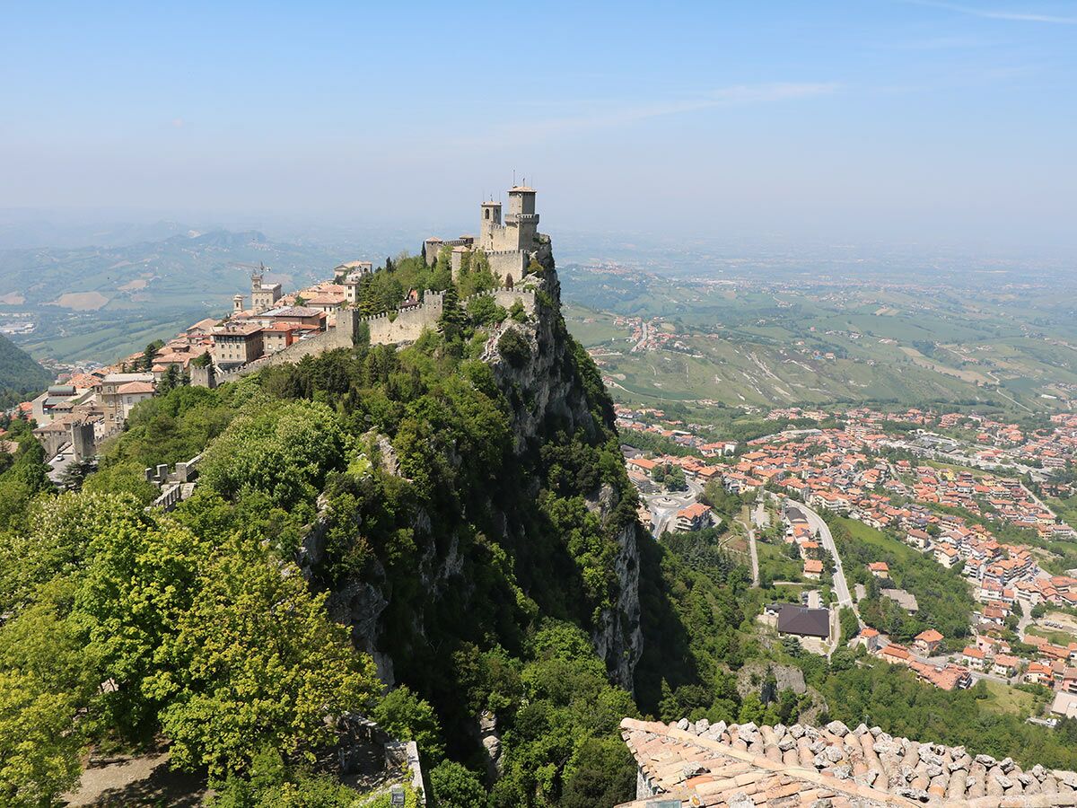 Historische Festungsstadt San Marino mit Burgtürmen auf steilem Felsen, umgeben von grüner Landschaft und Weitblick.