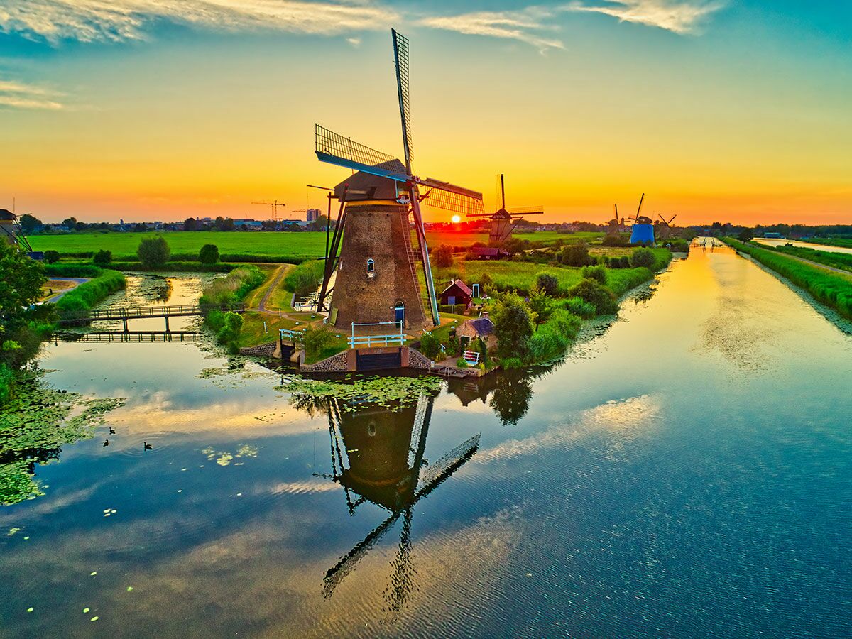 Panoramablick auf Windmühlen in Kinderdijk, Niederlande, bei Sonnenuntergang mit farbenprächtigem Himmel und Reflexionen im Kanal.