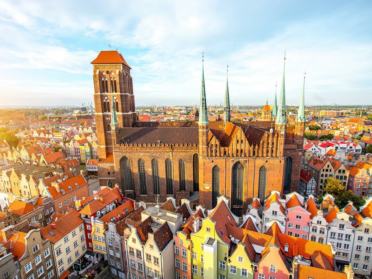 Luftbild von Gdańsk mit der imposanten St. Marienkirche und farbenfrohen Häusern im historischen Zentrum bei Sonnenlicht.