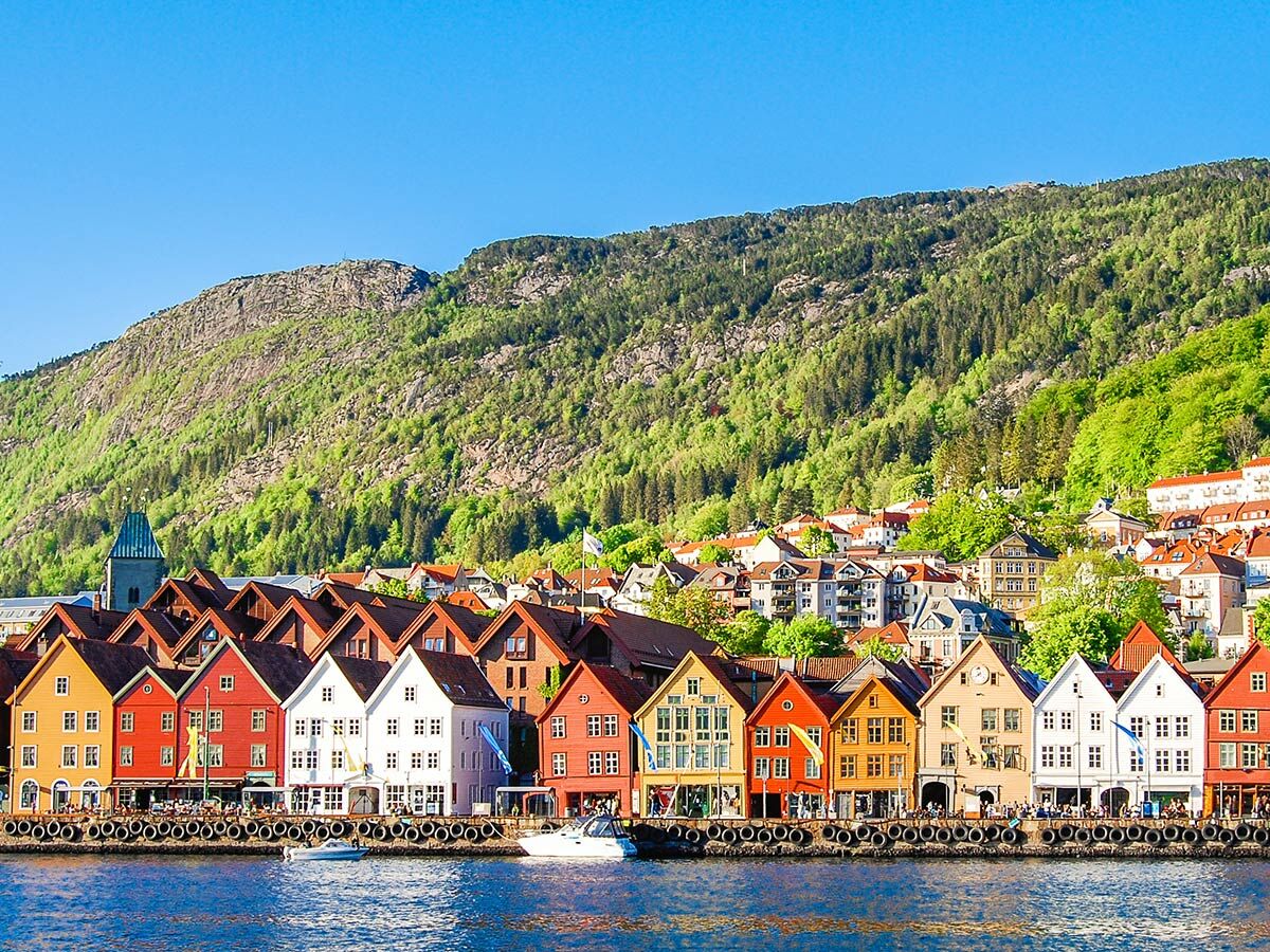 Panoramablick auf Bryggen in Bergen, Norwegen, mit farbenfrohen Holzhäusern am Hafen und bewaldeten Bergen im Hintergrund.