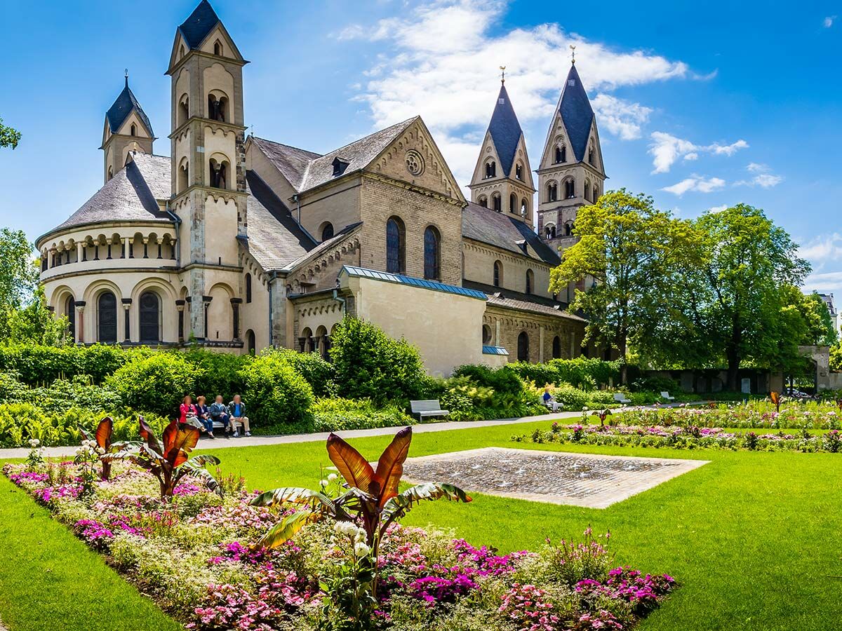 Historische Groß St. Martin Kirche in Köln mit blühendem Park und blauem Himmel an einem sonnigen Tag.