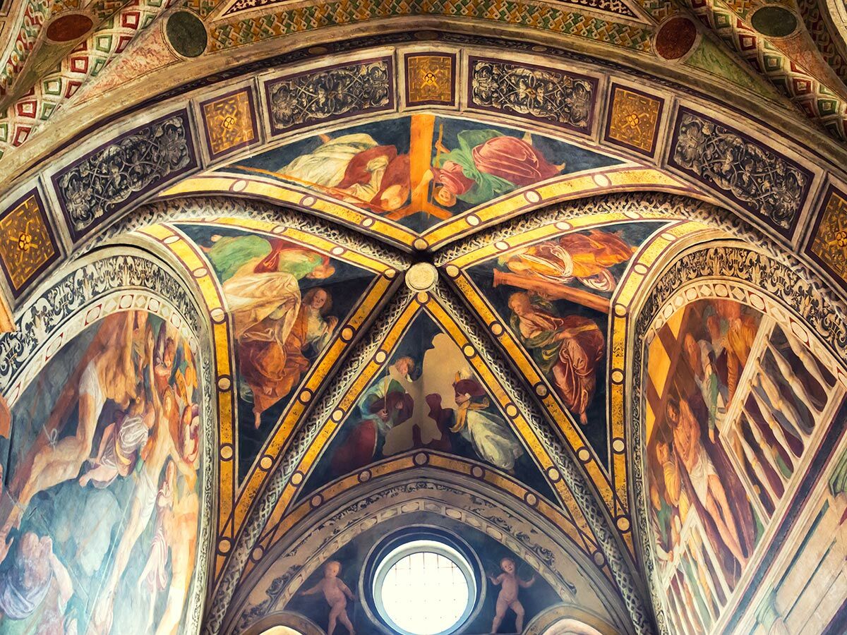 Gewölbte Kirchendecke mit farbenprächtigen Fresken, die biblische Szenen und Figuren zeigen, umgeben von ornamentalen Mustern.
