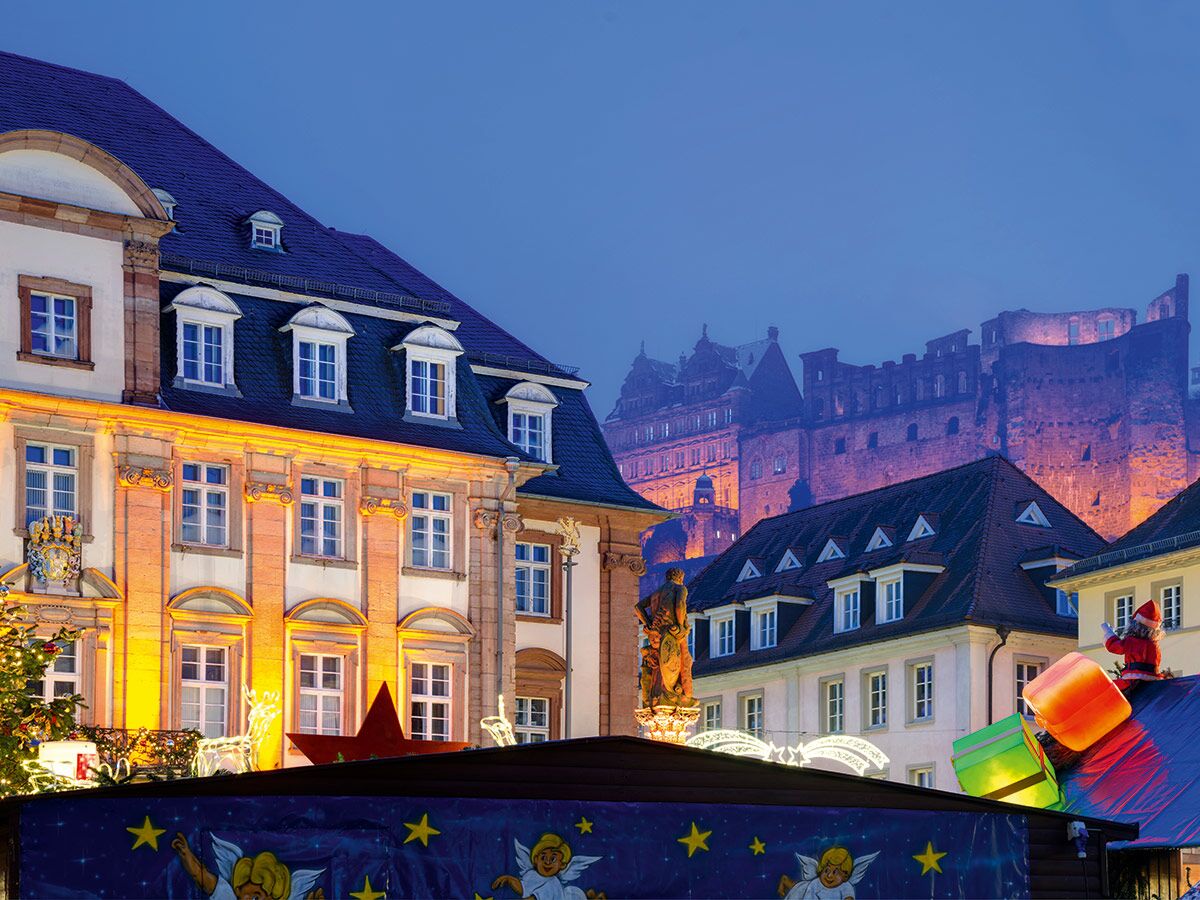 Festlicher Heidelberger Weihnachtsmarkt mit beleuchtetem Schloss, historischen Gebäuden, Marktständen und Winterdekoration bei Dämmerung.