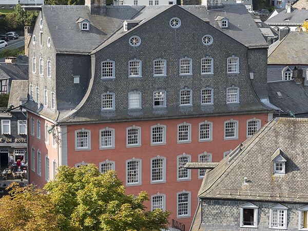 Großes historisches Gebäude mit markantem Schieferdach, runden Fenstern und roter Fassade in einer europäischen Stadtansicht.