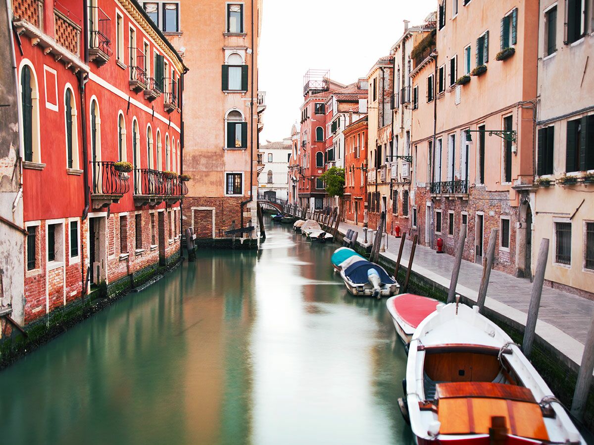 Blick auf einen malerischen Kanal in Venedig mit bunten, historischen Gebäuden und Booten im ruhigen, reflektierenden Wasser.