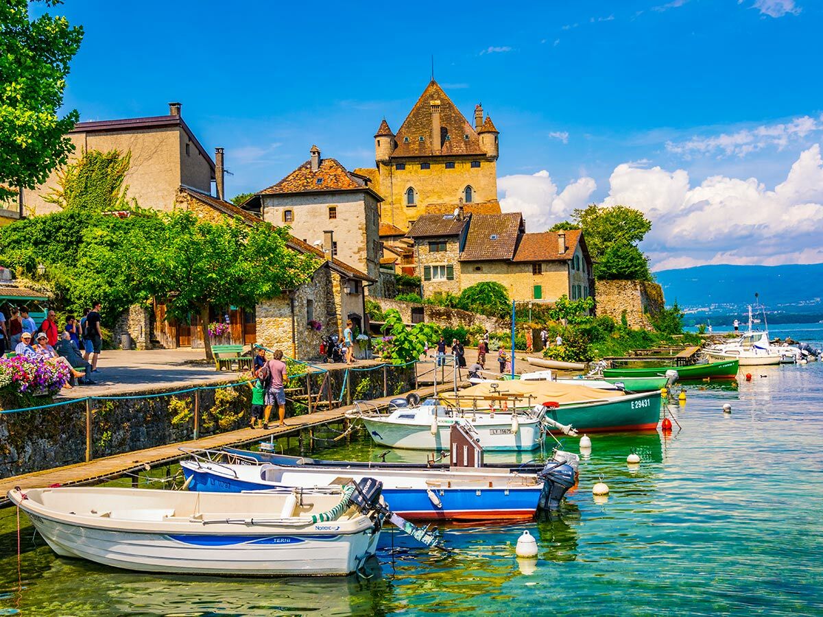 Malerisches Dorf Yvoire am Genfersee mit historischer Burg, Steinhäusern, vielen Booten am Steg und Bergen.