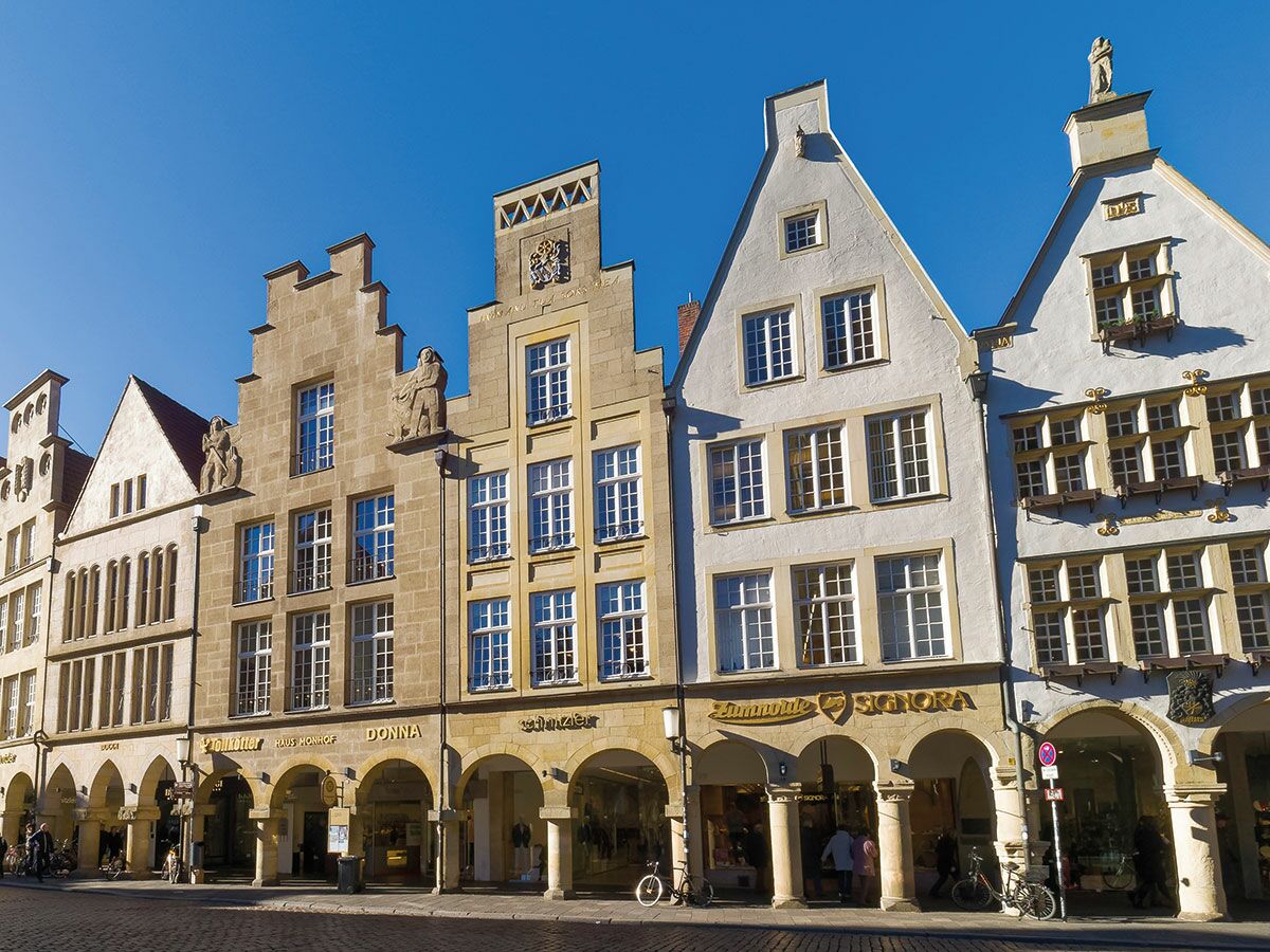 Reihe historischer Giebelhäuser mit Geschäften im Erdgeschoss unter blauem Himmel in der Altstadt von Münster.