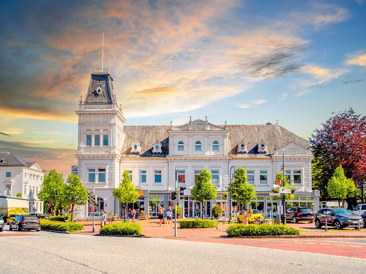 Elegantes weißes historisches Gebäude mit Turm an einem belebten Stadtplatz mit Autos und Menschen bei Sonnenuntergang.