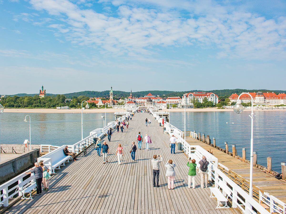 Langer Holzsteg der Sopot Seebrücke an der polnischen Ostsee mit zahlreichen Spaziergängern und dem Grand Hotel im Hintergrund bei Sonnenschein.