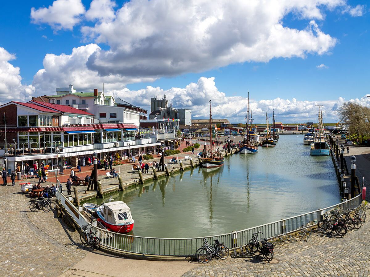 Belebter Hafen einer Küstenstadt mit traditionellen Booten, Restaurants und vielen Menschen am Kai unter blauem Himmel.