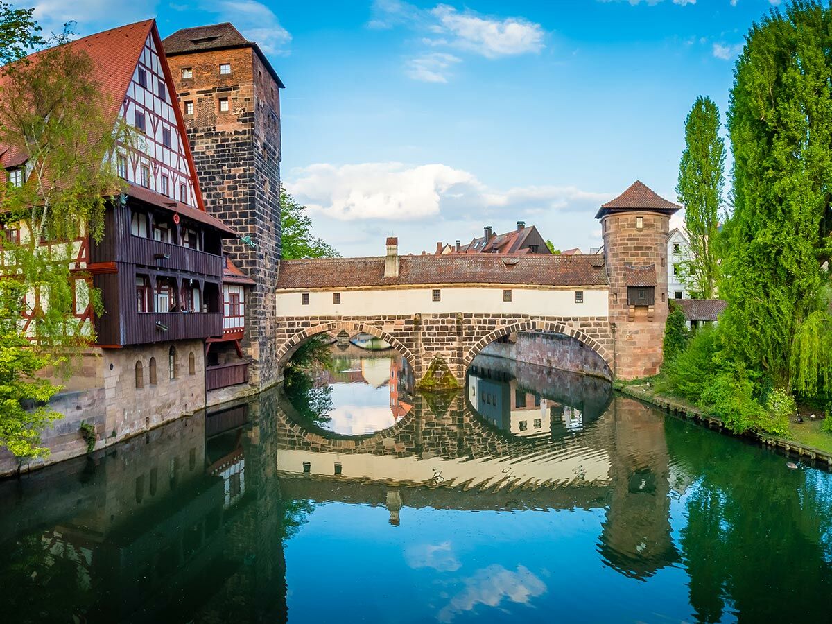 Historische Altstadt Nürnberg am Pegnitz-Fluss mit Weinstadel, Henkersteg und blauer Himmelsreflexion im Wasser.
