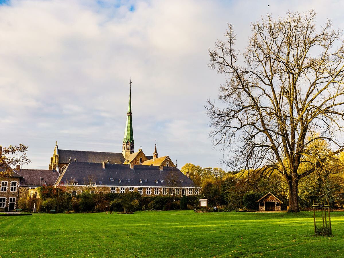 Historisches Kloster mit markantem grünem Kirchturm in einem herbstlichen Park mit großer Wiese und kahlen Bäumen.
