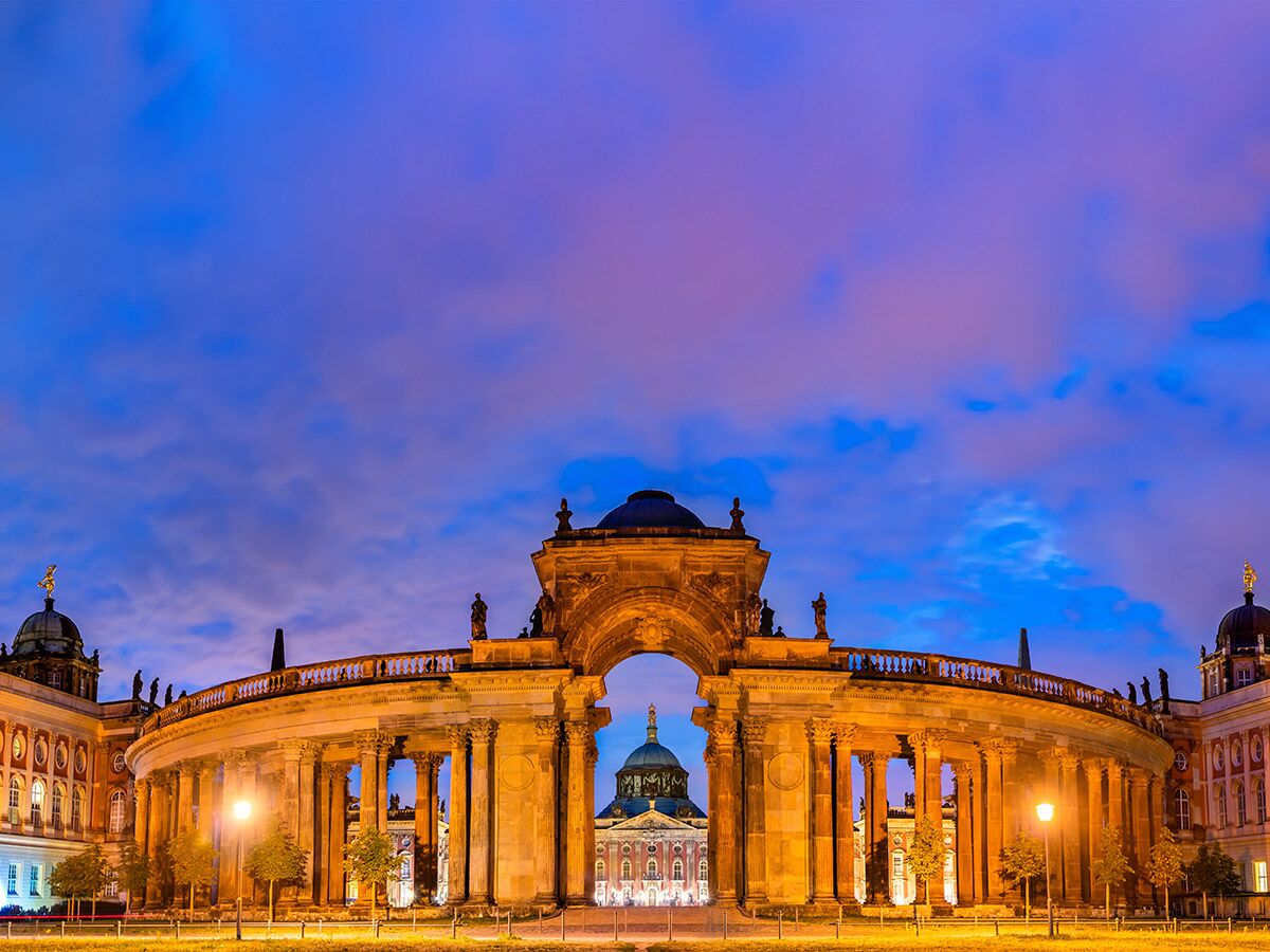 Das Neue Palais in Potsdam bei Dämmerung, prächtige Barockarchitektur mit beleuchteten Säulen und Kuppeln unter blau-violettem Himmel.