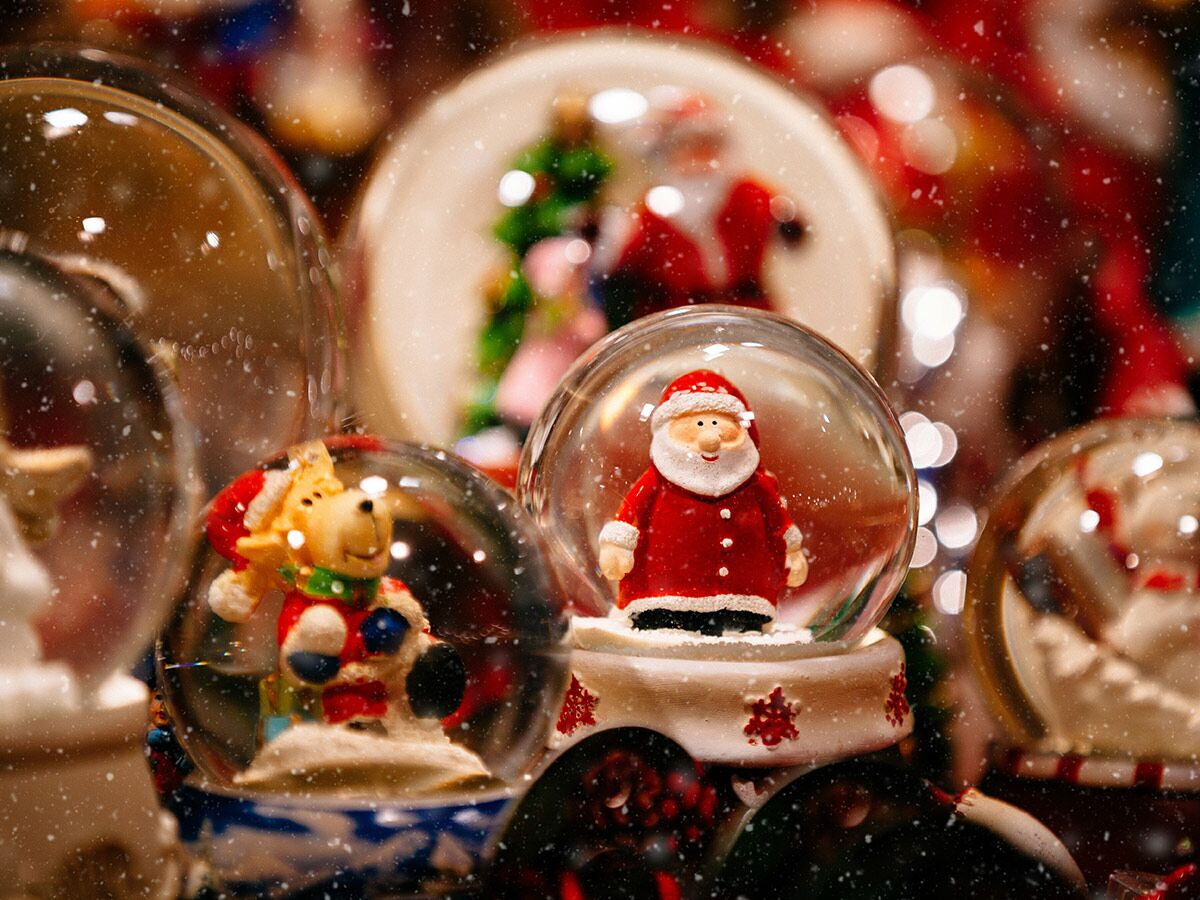 Nahaufnahme festlicher Schneekugeln mit Weihnachtsmann und Rentier, umgeben von funkelndem Schnee und bokeh Lichtern.