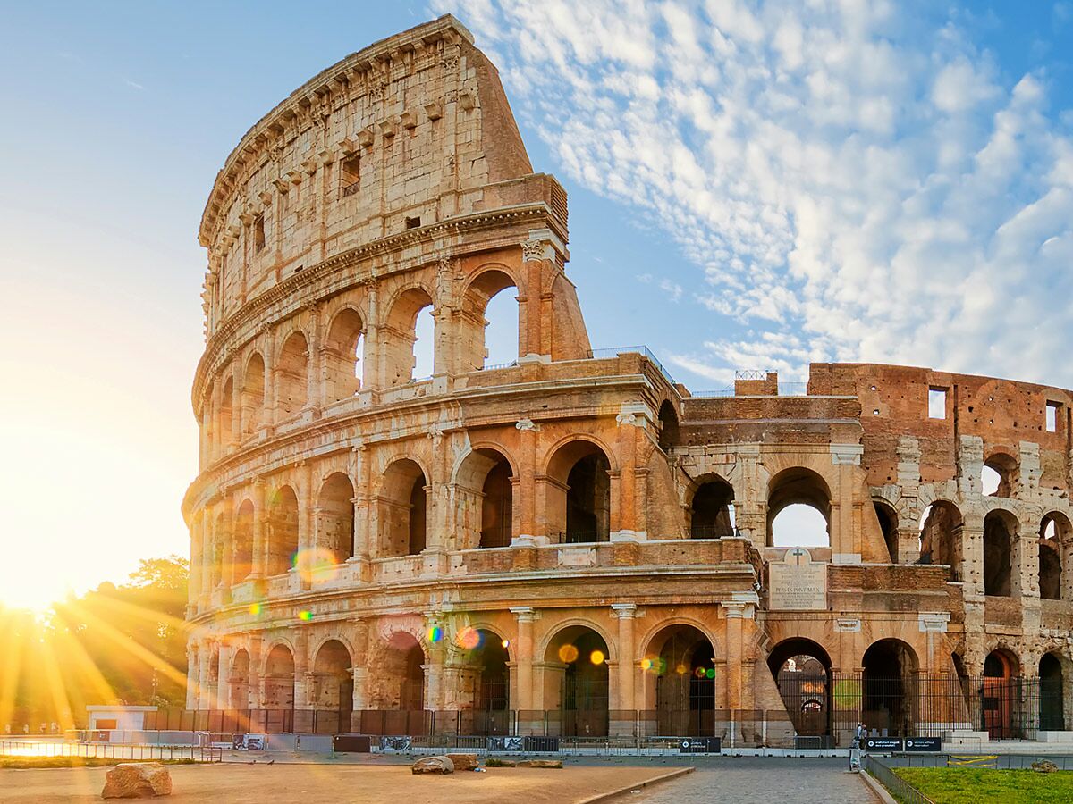 Das Kolosseum in Rom, Italien, bei Sonnenaufgang. Goldene Sonnenstrahlen beleuchten die antike römische Arena unter blauem Himmel.